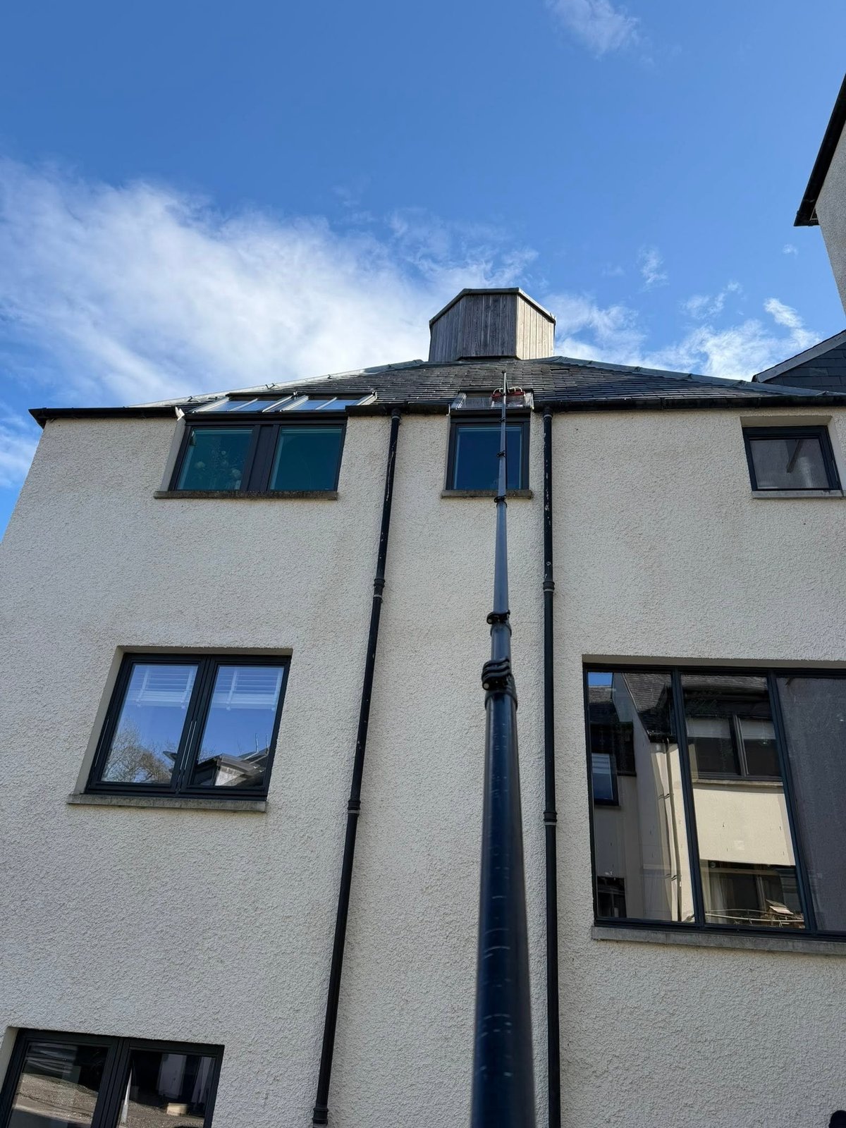 White residential building with multiple windows and a vertical black drainpipe against a blue sky